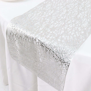 Silver lace table runner with intricate design on a white tablecloth.