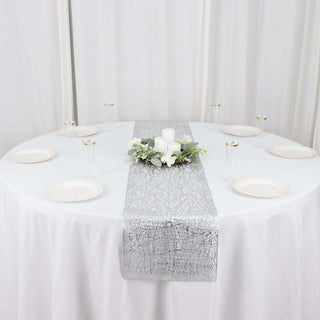 Elegant silver table runner on a round table with candles and floral accents.