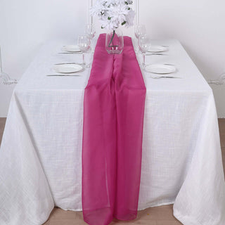 Pink table runner on a white table set for dining with plates and glasses.