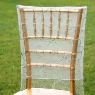 Gold chiavari chair with sheer lace cover against green grass backdrop.