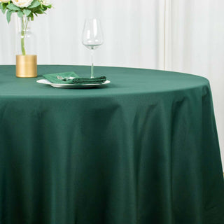 Green round tablecloth on a dining table with decorative elements and glassware.