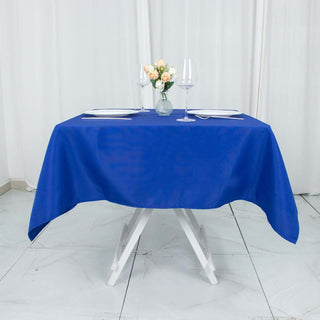 Blue tablecloth on a dining table set for two with flowers and glassware.