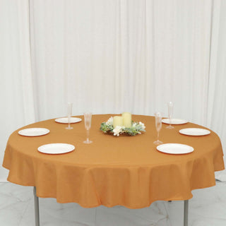 Round table set with orange tablecloth, plates, and candles.
