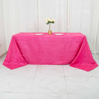 Pink tablecloth draped over a table with plates and a vase of flowers.