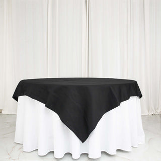 Black tablecloth draped over a white table with a backdrop of white curtains.