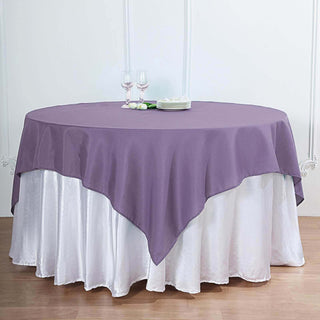 Purple tablecloth draping over a white table with glasses and plates on top.