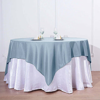 Round table with a blue tablecloth and white satin overlay, elegantly styled.