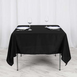 Black tablecloth on a dining table set with glasses and plates.