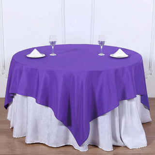 Purple round tablecloth draped over a white table with glasses and napkins.