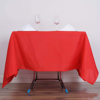 Red tablecloth with wine glasses and napkins set on a table.