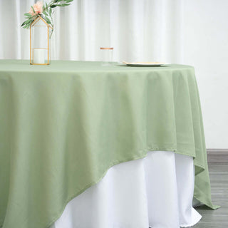 Green tablecloth draping elegantly over a white table with a vase and glass on top.