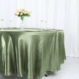 Green satin tablecloth draped over a round table with elegant dinnerware and flowers.