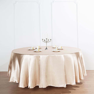 Round satin tablecloth in champagne color with plates and a candelabra.