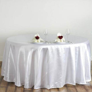 Elegant round table set with white satin tablecloth and romantic place settings.