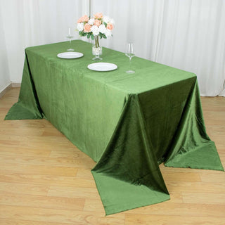 Green tablecloth draped on a table with plates and flowers.