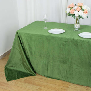 Green tablecloth draped over a table with plates and flowers.