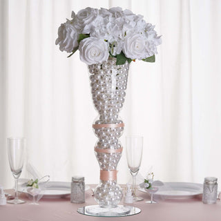 Elegant floral centerpiece with white roses and pearl accents on a table.
