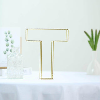 Gold letter "T" decorative sculpture on a table with plants in the background.