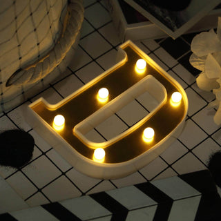 Decorative marquee letter "D" with warm lights on a patterned surface.