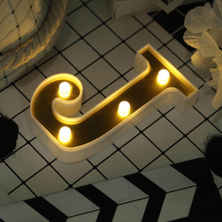 Illuminated decorative letter "J" with warm lights on a patterned surface.