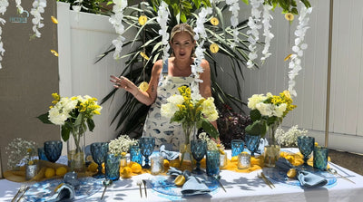 Amalfi Coast summer table setup featuring blue glassware and vibrant flowers.