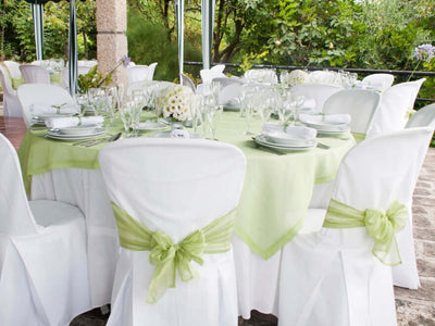 Outdoor banquet table with white chair covers and green tablecloth