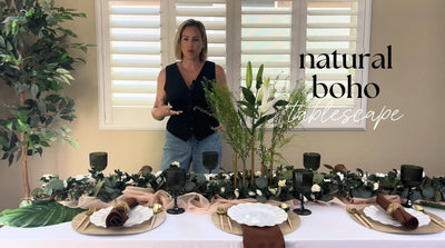 Finished natural boho tablescape with black glasses and green floral decor.