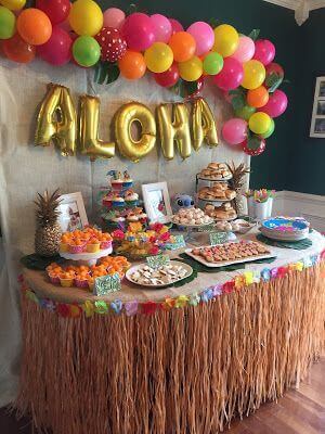 A tropical party table with aloha balloons and buffet spread