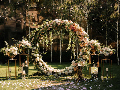 Outdoor floral arch with string lights and pedestal arrangements