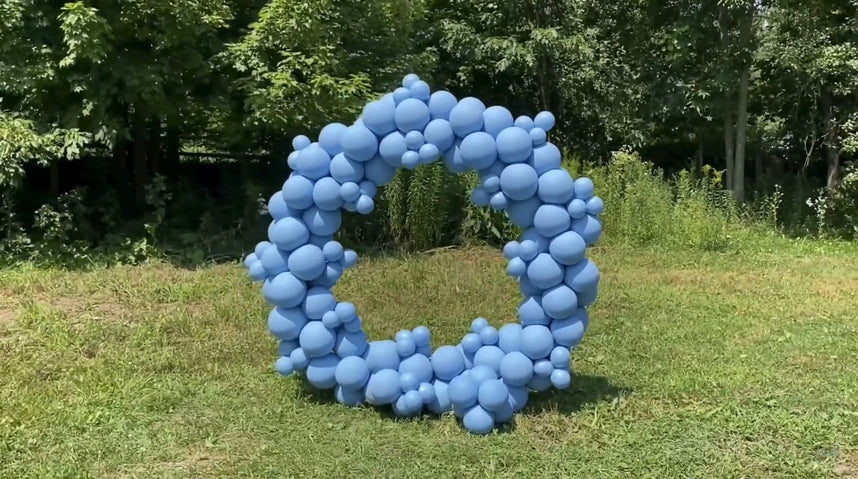 Fully completed circular blue balloon arch displayed on grass outdoors.