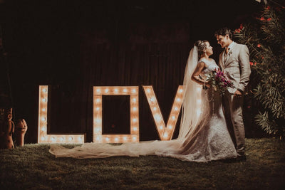 Bride and groom standing before illuminated LOVE letters