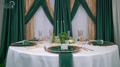 Elegant green and gold table decor with charger plates, candles, and glassware.