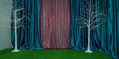 Dual lighted birch trees with teal velvet and burgundy sequin backdrops on green grass carpet.