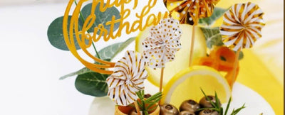 Cake topper with gold birthday lettering and paper pinwheels