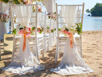 White chairs with floral sashes on a beach wedding setup