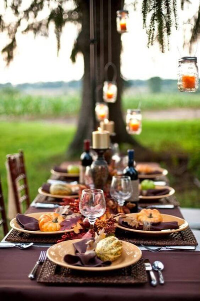 Outdoor Friendsgiving table setting with candles and mini pumpkins