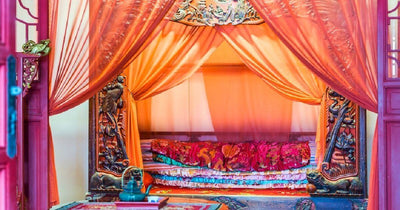Sheer orange drapes around a bed
