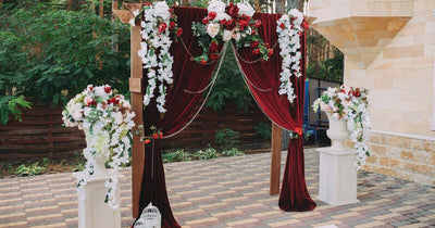 Wedding arch with burgundy drapes and white floral arrangements