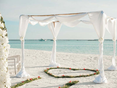 White draped wedding backdrop on a beach
