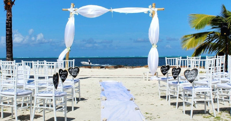 Beach wedding ceremony with white draped arch