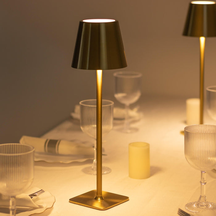 Elegant gold table lamp illuminating a dining setting with glasses and candles.