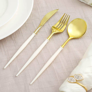 Gold cutlery set with white handles on a textured tablecloth.