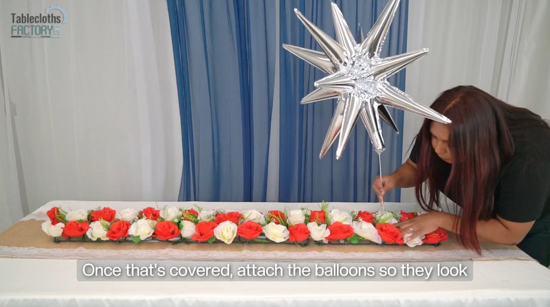 Attaching silver star balloons above 4th of July table setup with floral runner.