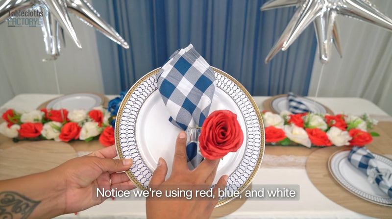 Hand places plate with blue napkin and red rose for 4th of July table setup.