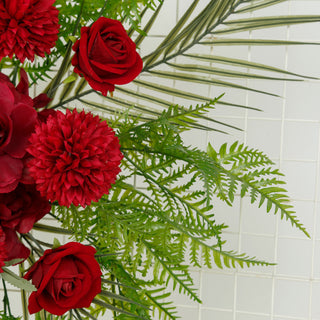 Red roses and green ferns in a floral arrangement.
