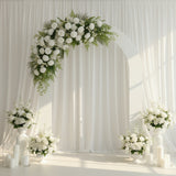 White floral arch with arrangements and candles in a serene setting.