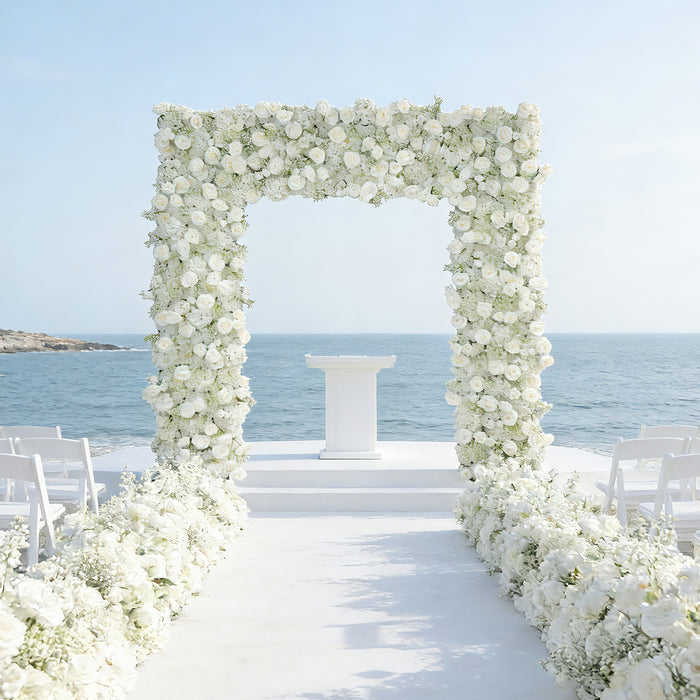 Elegant floral wedding arch by the sea with white flowers and chairs.