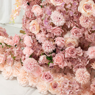 Pink floral arrangement with roses and assorted blooms on a neutral backdrop.