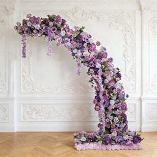 Purple floral arch arrangement with intricate blooms against a textured wall backdrop.