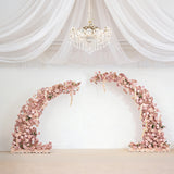 Floral installation arch in soft pink hues against a plain backdrop. 